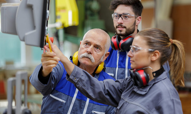 Eine Frau und zwei Männer an einer Produktionsmaschine